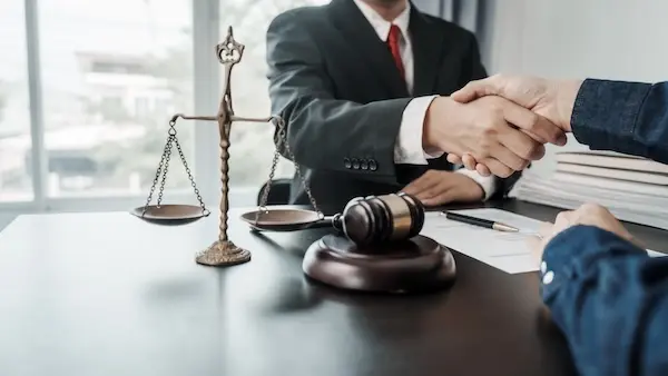 A motorcycle accident lawyer is shaking hands with a client at a desk.
